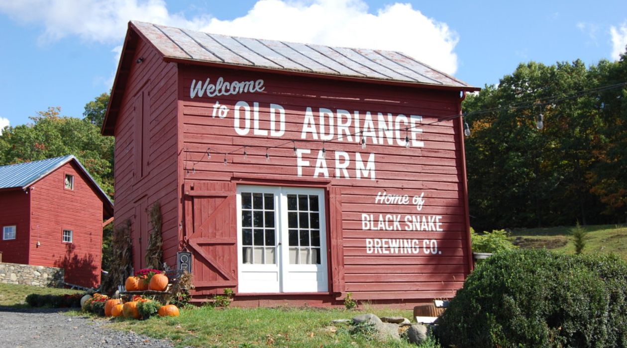 The red barn with a metal roof at Old Adriance Farm with pumpkins displayed next to it.